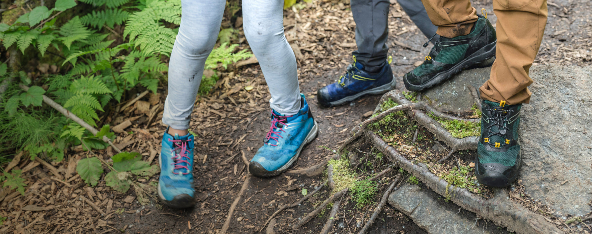 Knee down view of kids wearing wanduro shoes walking over treet roots