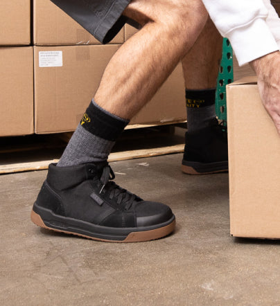 Knee-down shot of man wearing black Kenton mid work sneaker and moving cardboard boxes.