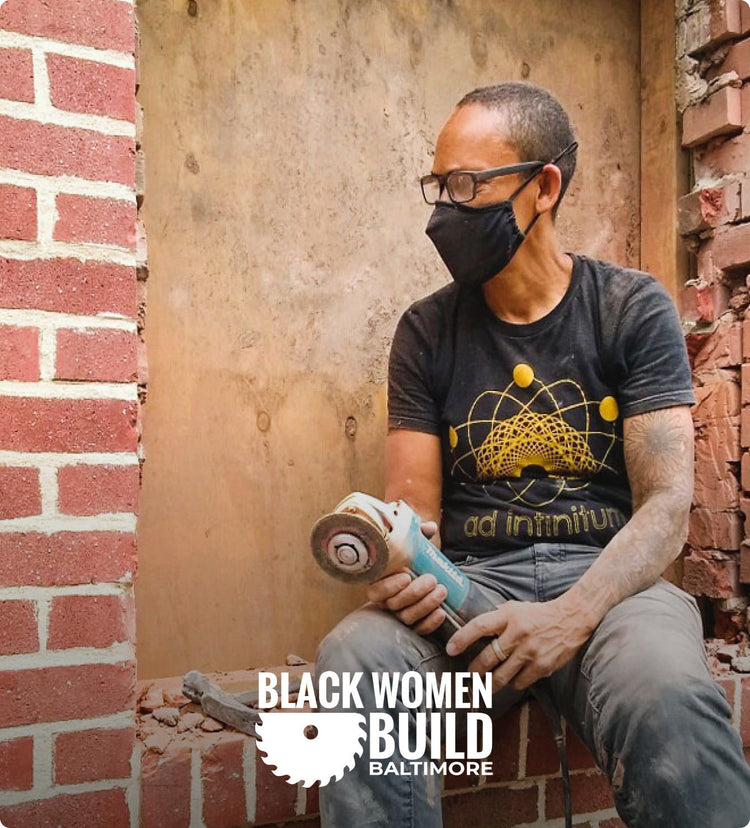 Woman wearing facemask and glasses holding grinder while workin on brick building 
