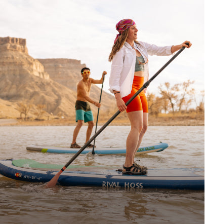 Man and woman in Newport sandals paddleboarding in a desert lake setting