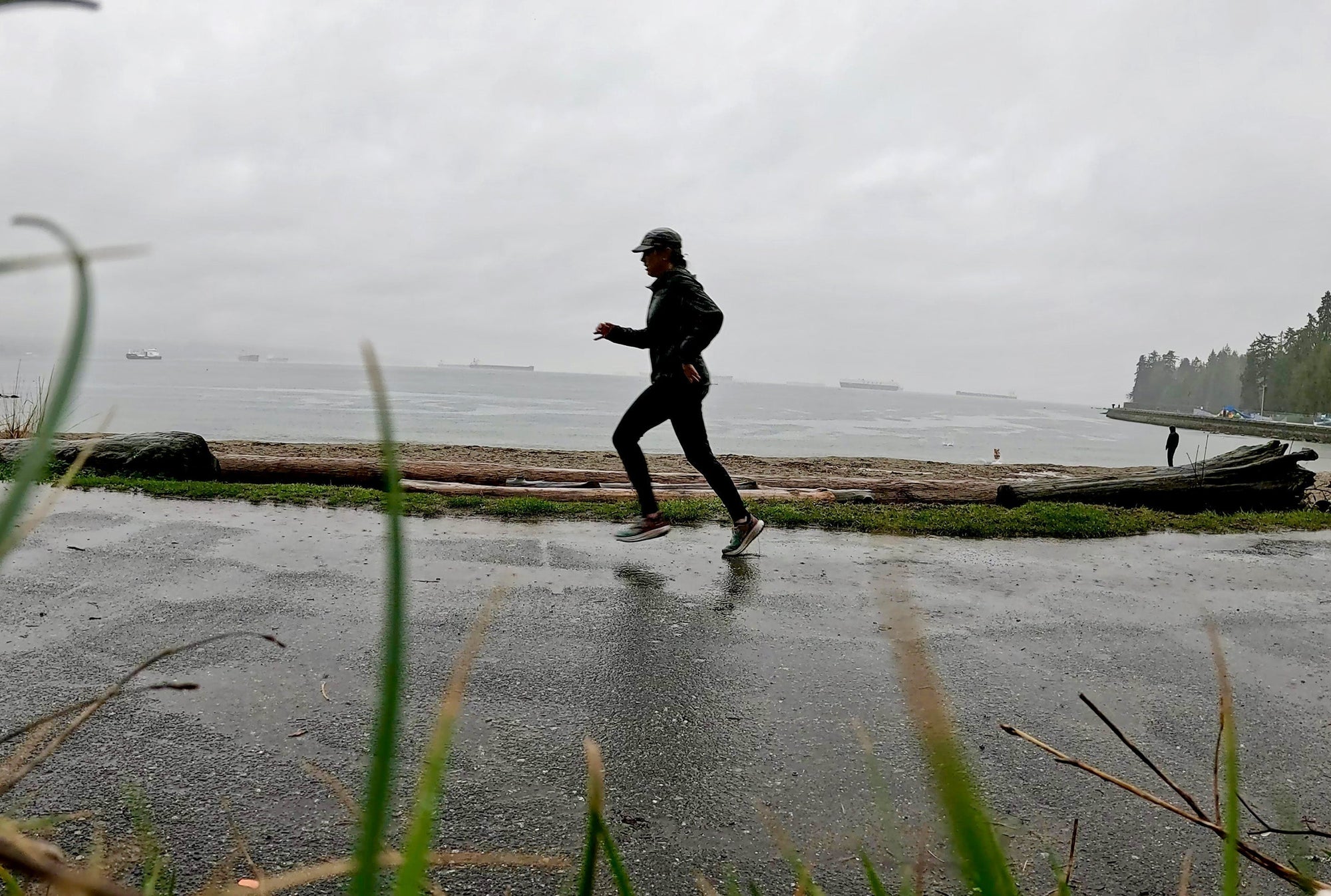 A woman running in the rain on a paved trail in Vancouver, Canada.