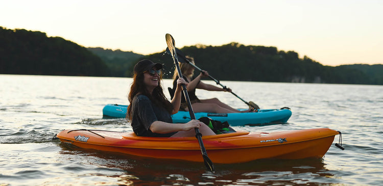 two people kayak on a flat lake at sunset