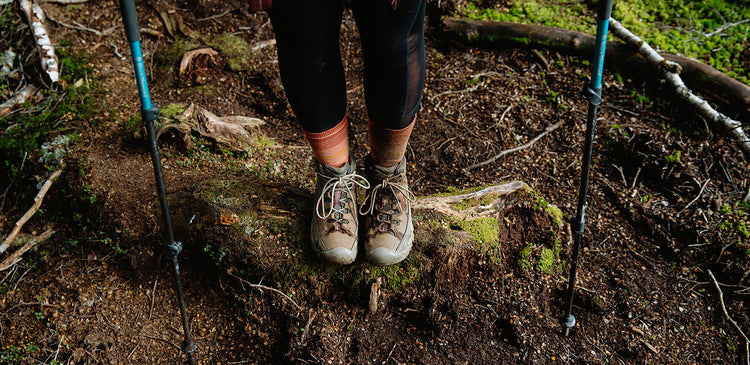 a pair of feet wearing Targhee boots stands on a trail between trekking poles