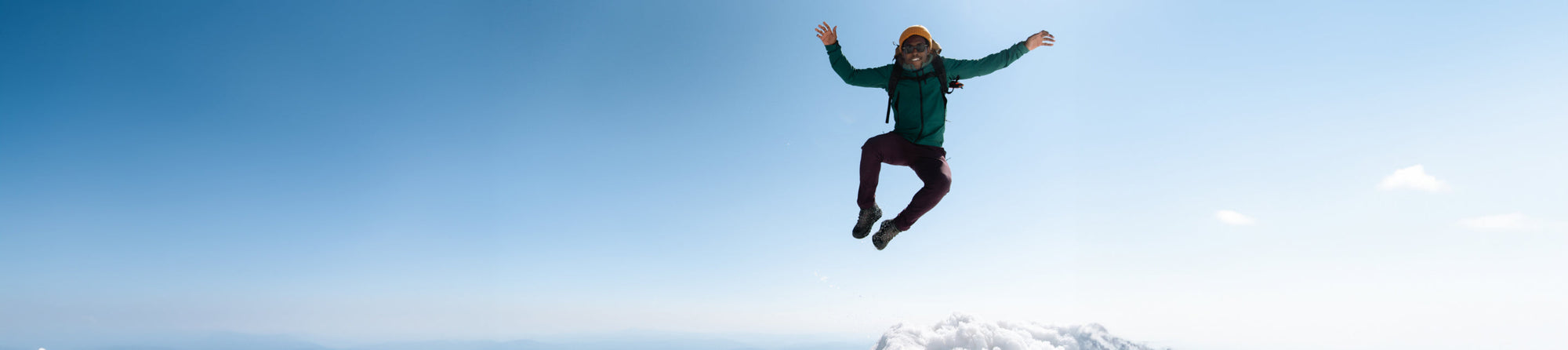 A banner image of someone jumping in the air wearing winter weather attire, boots, and a backpack, with a blue sky in the background.