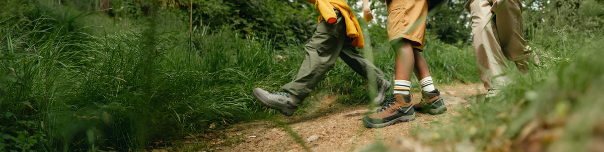 Three children running down a path outside, with many trees in the background.