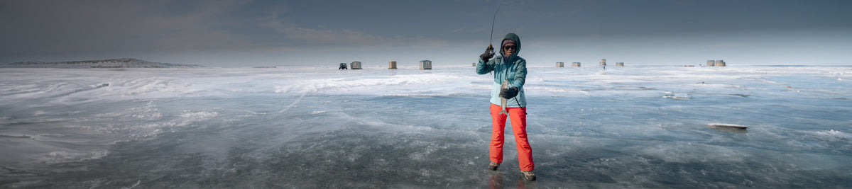Woman standing on ice, holding a fish, wearing winter apparel and boots