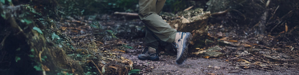 Someone shown from the knees down walking across forest terrain, wearing KEEN hiking sneakers.