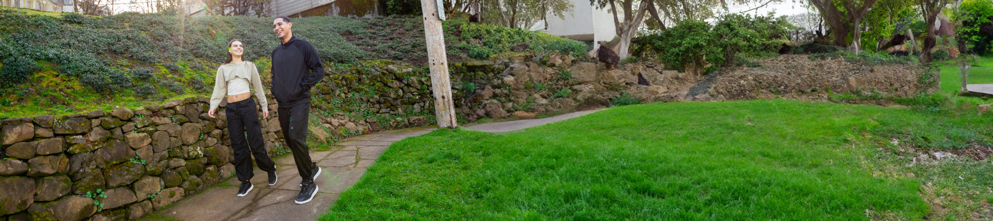 Banner image of a man and a woman walking along a stone path outside, wearing KEEN footwear