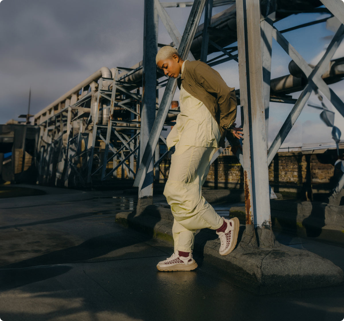 Person leaning up against metal building frame wearing off-white wearing white UNEEK walking sandals with red socks.