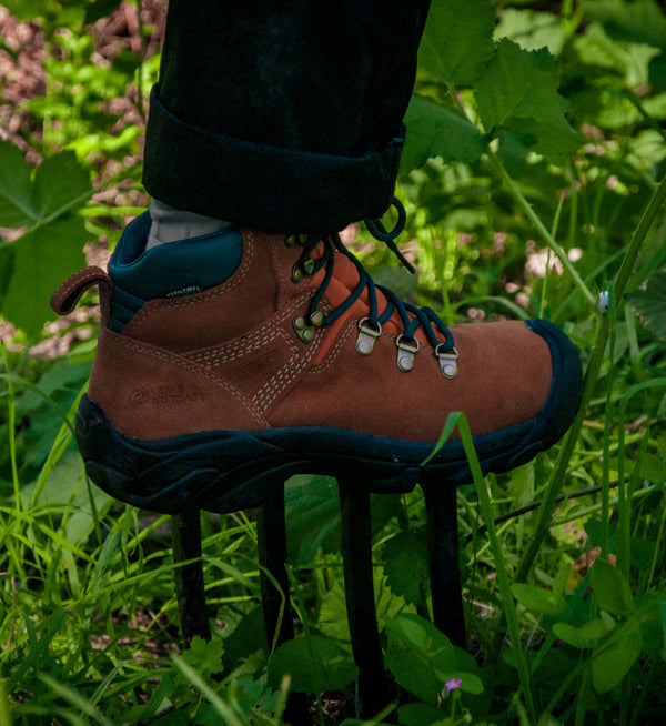 A person standing in grassy field, wearing a pair of brown KEEN boots.