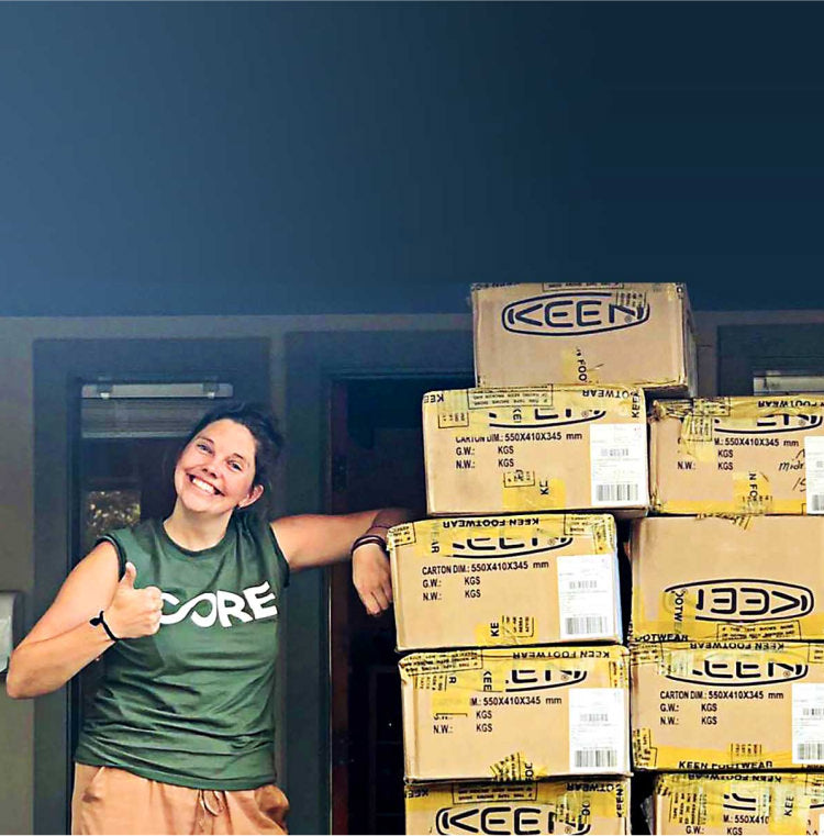 woman standing next to a pile of boxes filled with Keen shoe donations