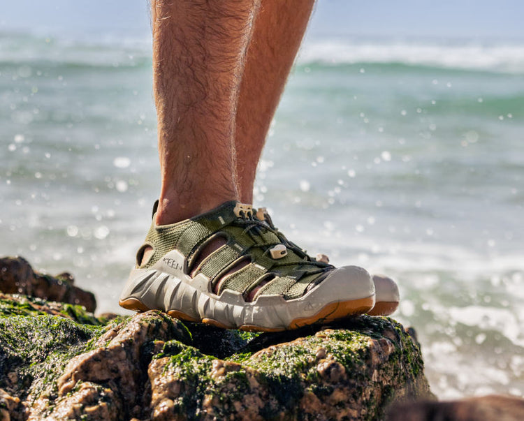 Knee-down shot of man wearing Hyperport H20 sandal and standing on a wet, ocean rock.