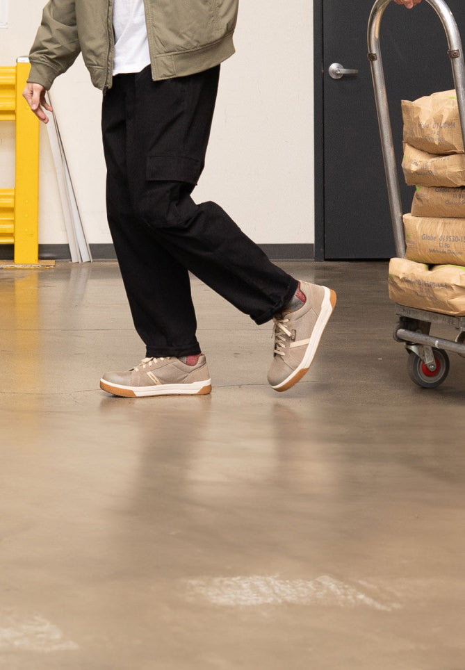 Knee-down shot of man wearing tan Kenton work sneakers and pulling a cart of brewing materials across warehouse floor. 