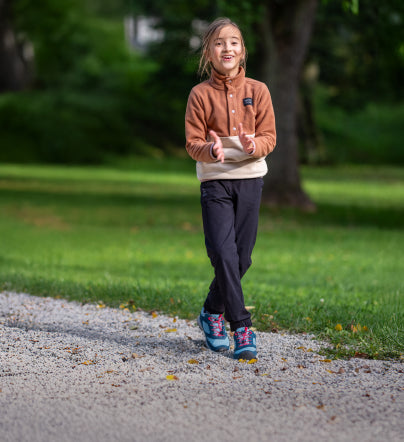 Little girl walking through grassy park on gravel trail while wearing Big Kids' 
 blue and pink Skua Waterproof Shoe  
