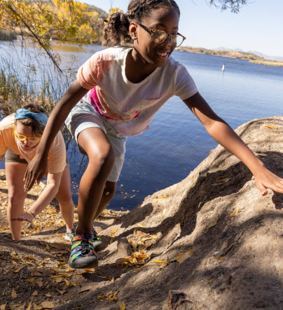 Two girls wearing Newport Sandals climbing up rocky trail in front of lake