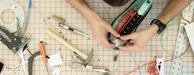 A person's hands using laces to build a shoe on a craft table with scissors and a ruler 