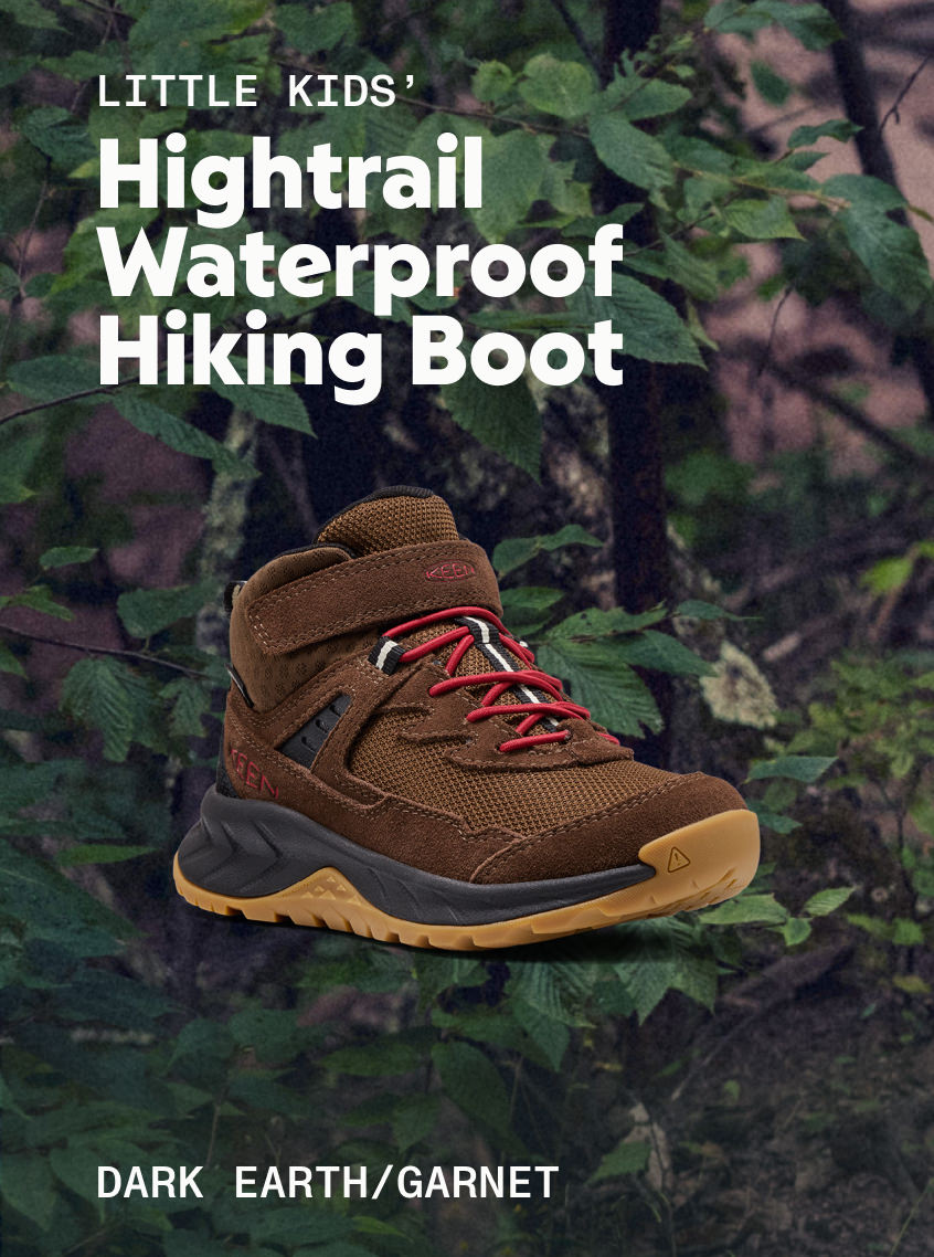 Product shot of Little Kids' Hightrail Waterproof Hiking Boot in Dark Earth and garnet against leafy trees.