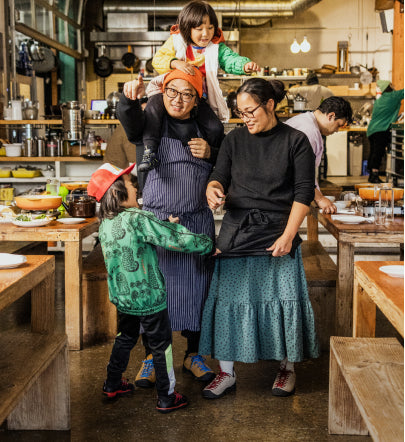 2 young kids talking to parents wearing aprons in restaurant setting