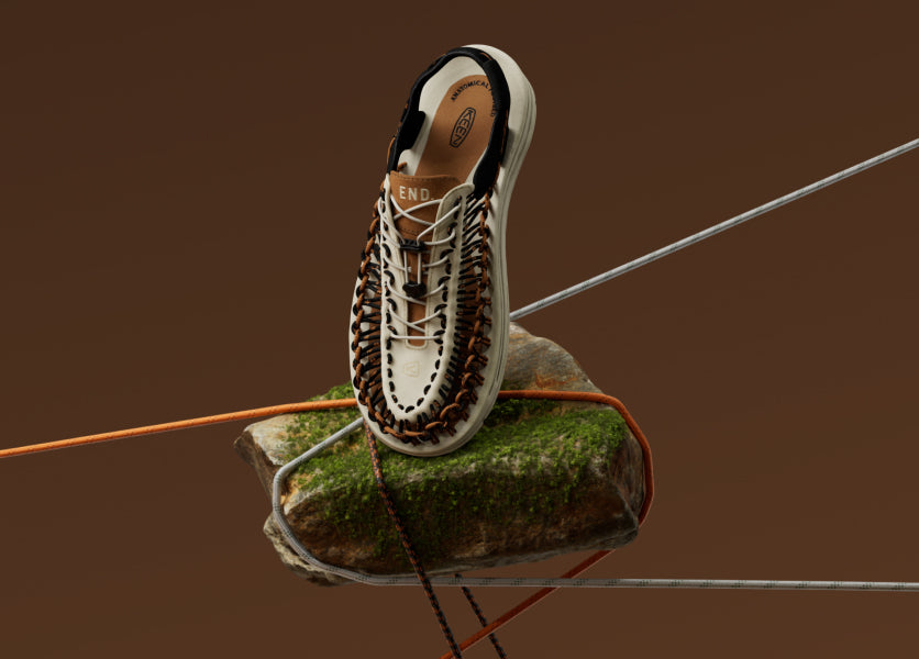 Product shot of End and KEEN collaborations Uneek sandal on small grass patch with orange and blue elastic thread detail