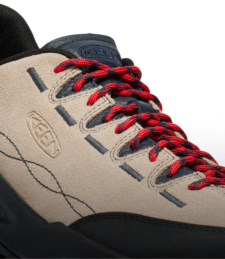 A close-up of a brown and black KEEN sneaker with red shoe laces.