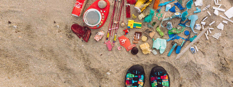 Newport sandals next to a pile of trash on the beach that has been sorted by color. 