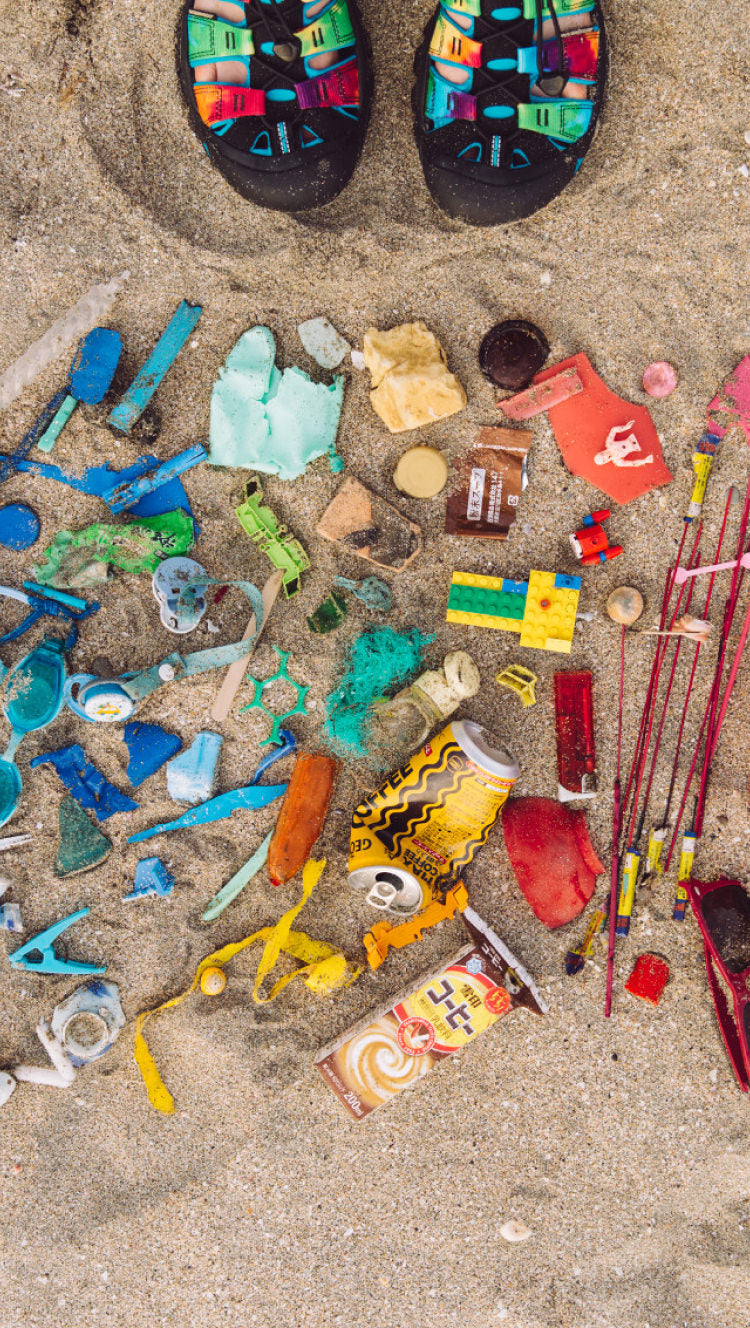 Newport sandals next to a pile of trash on the beach that has been sorted by color. 