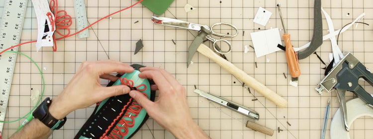 hands adding laces to a shoe that is being built on a craft table with scissors and a ruler.