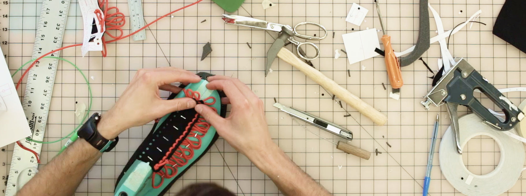 A person's hands working on threading the cords of a Uneek sandal on a grided project table