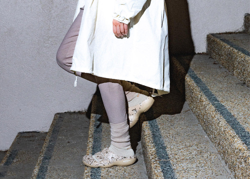 A person walking down stairs, wearing a pair of KEEN Yogui clogs.