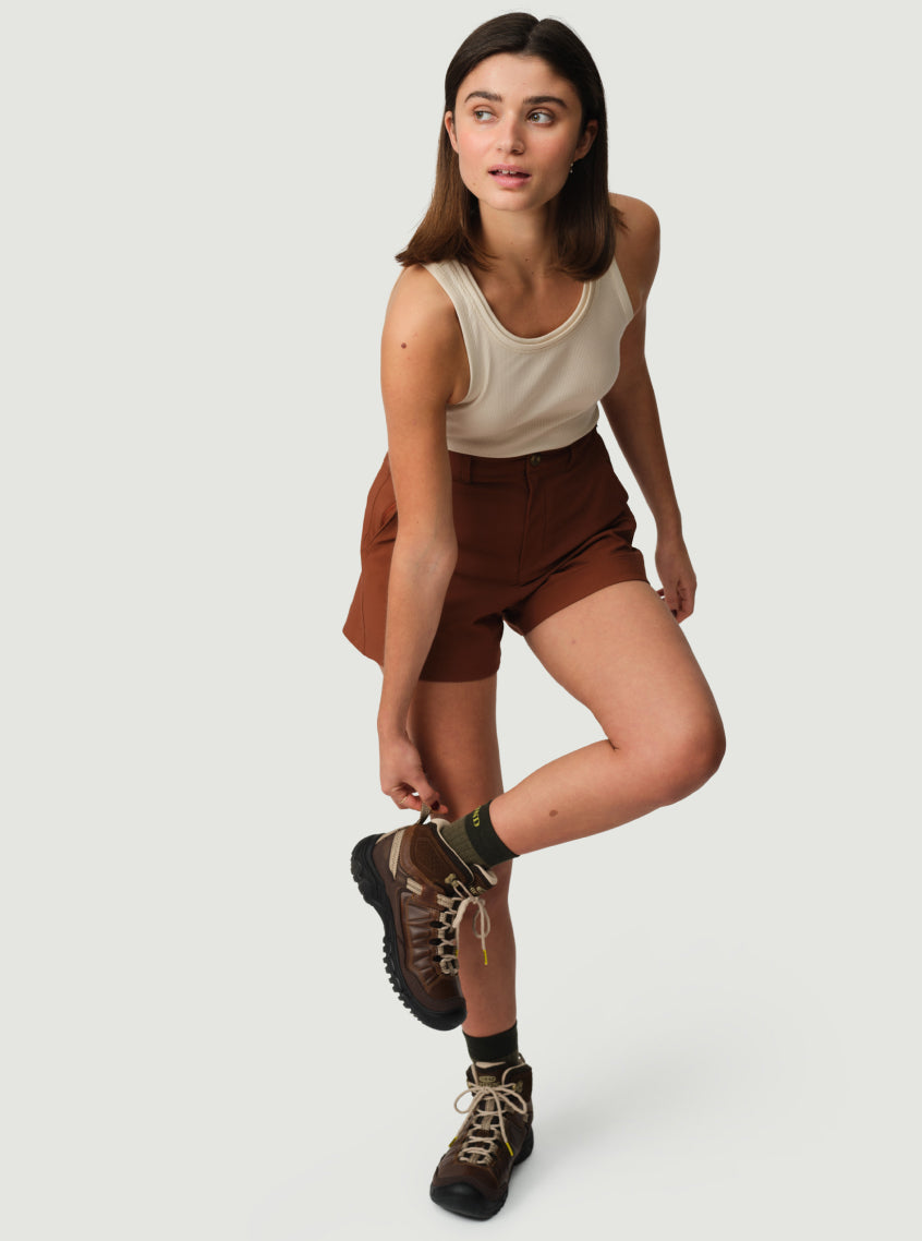 Woman in summer hiking clothes putting on brown leather Hikerkind and Keen collaboration boots