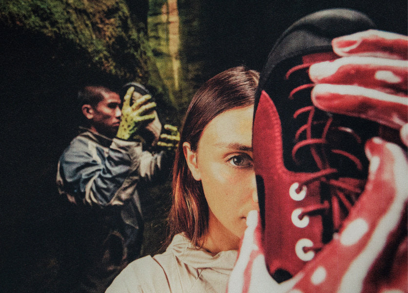 Woman with red paint on her hands holding up the KEEN and Hiking Patrol collaboration Jaspers shoes in front of one of her eyes. 