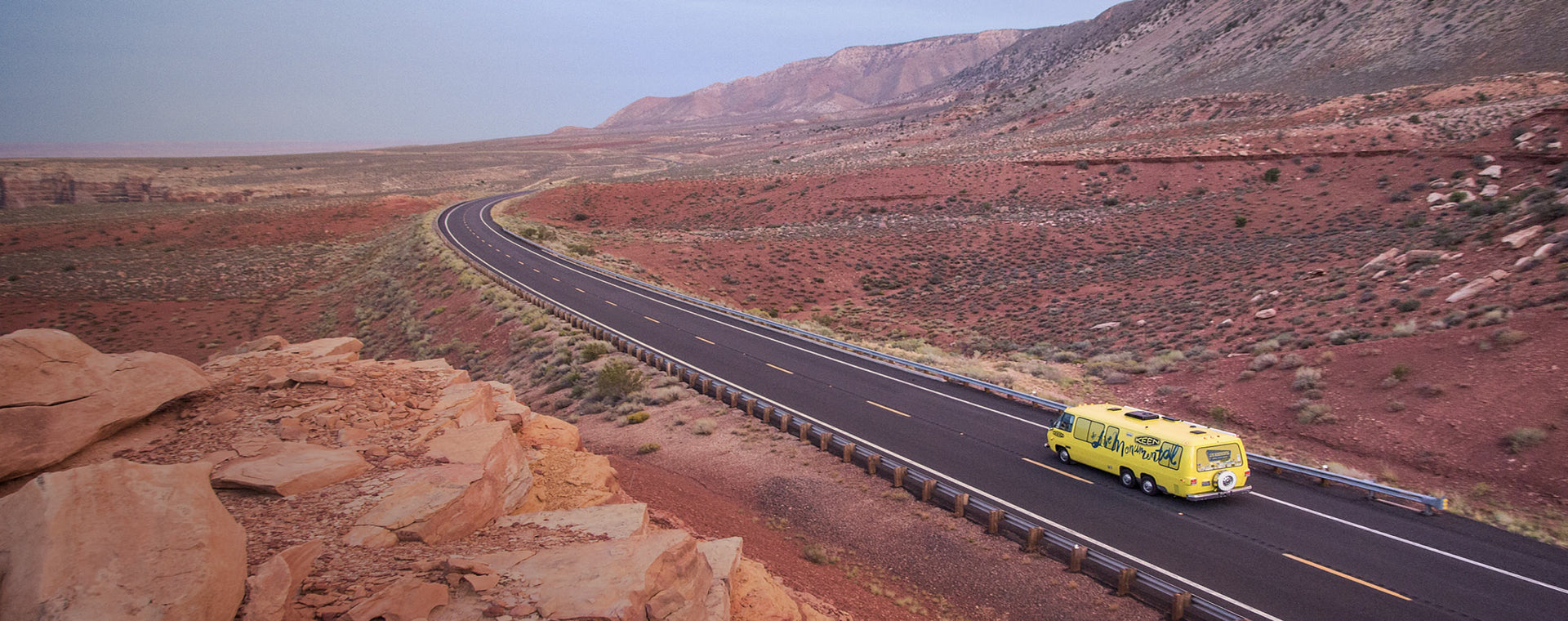 Yellow Keen bus driving through red, mountainous desert landscape
