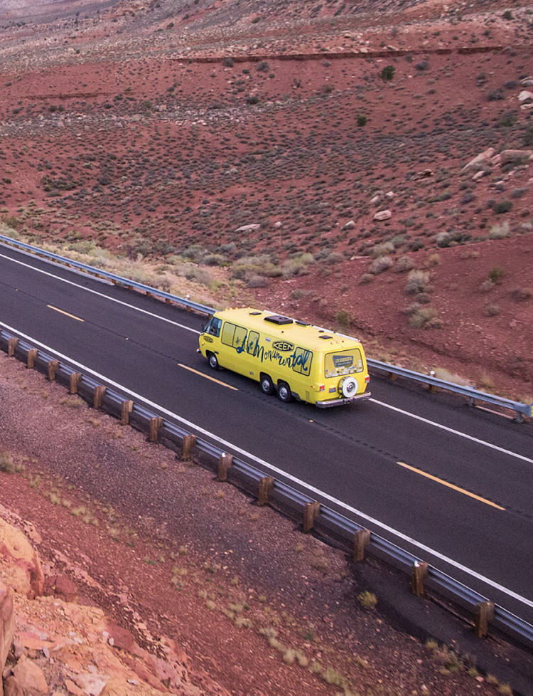 Yellow Keen bus driving through red, mountainous desert landscape