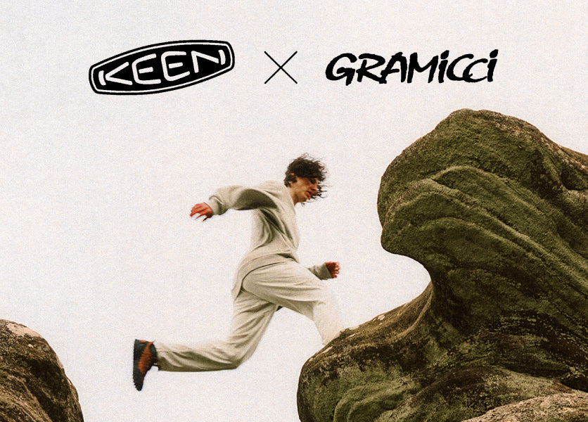 Photo of man in a cream colored casual sweatsuit, wearing red Gramicci collaboration Jasper Zionic sneakers and jumping from one large rock to another. 