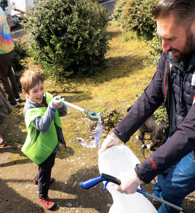 A man helping a young boy put trash into a white garbage bag outside.