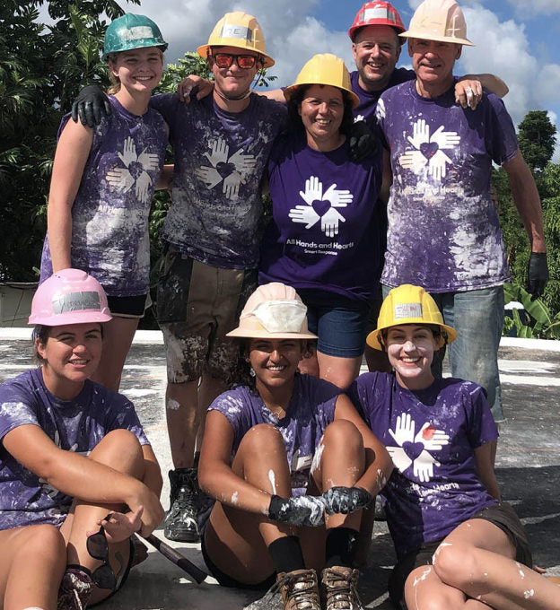 A group of people in hard hats and matching purple t-shirts, smiling for a photo.