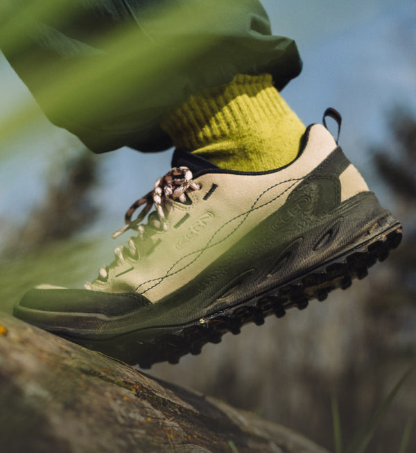 A person wearing the Jasper Zionic sneaker in tan suede while walking up a steep rocky surface.