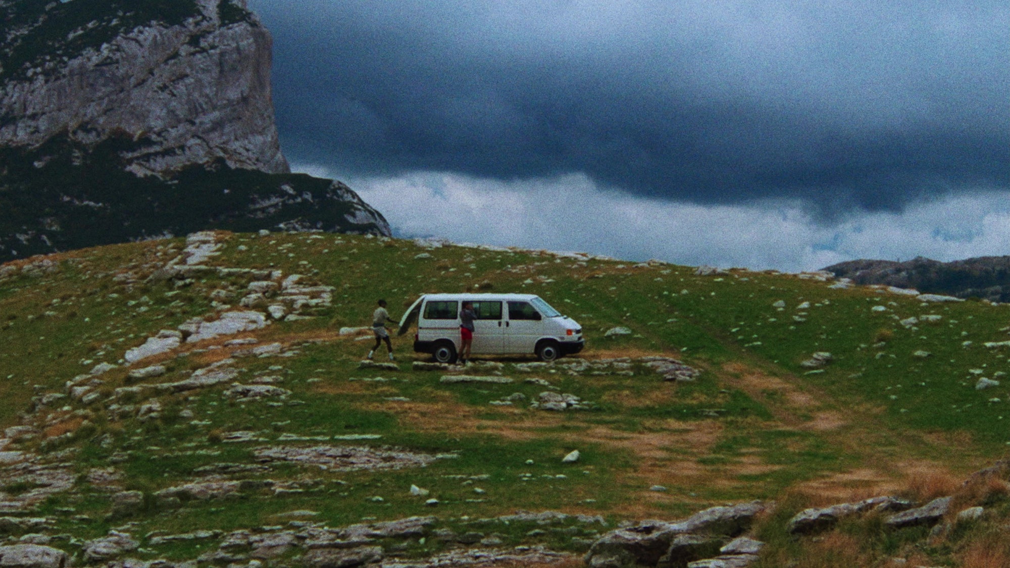 A man and woman leaving their van to head out on a trail run over grassy and rocky plains. 