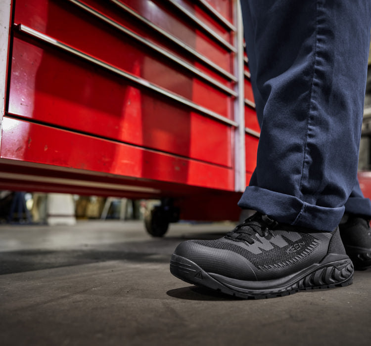 A person wearing a pair of black KEEN work sneakers.