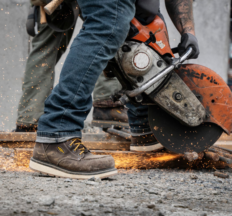 A person operating machinery on a job site, wearing KEEN work boots.