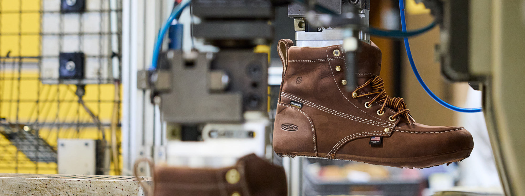 Leather work boot with "American built" flag in focus being created on shoe manufacturing machine. 