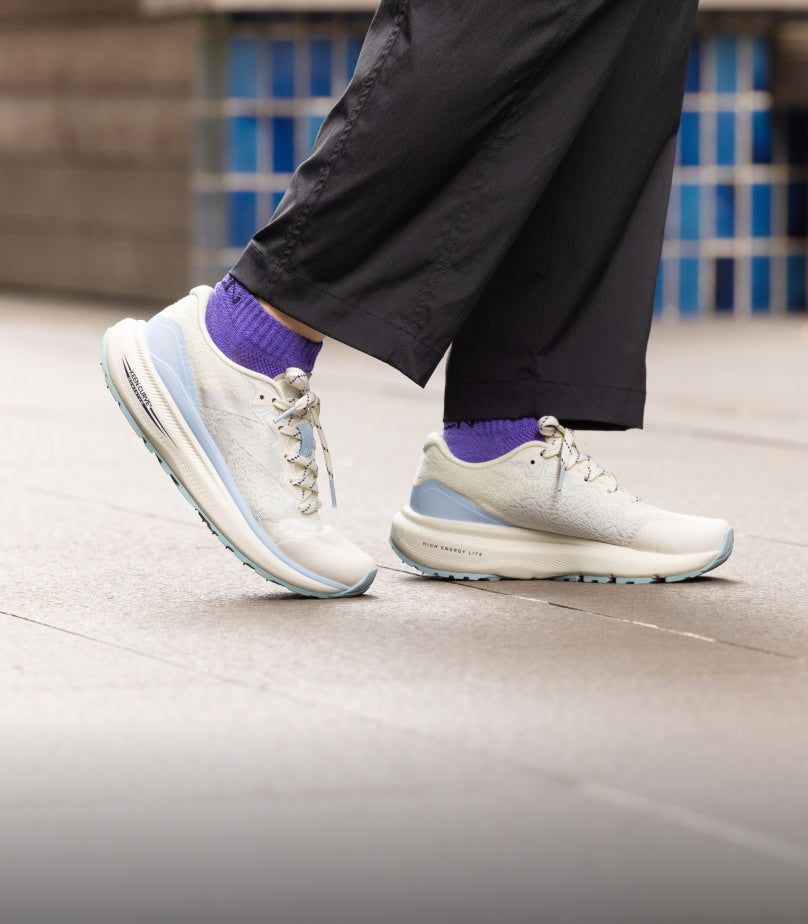 Knee-down shot of woman wearing white and light blue WK500 walking shoes with purple socks and black pants.