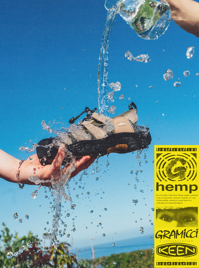 Product shot of tan and black KEEN and Gramicci collaboration Newport sandal against blue sky with water being poured on it from glass pitcher.
