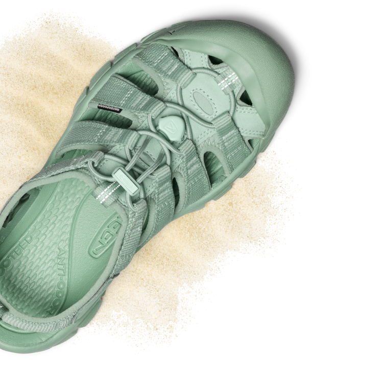 Product shot of light turquoise monochrome Newport water sandal with tan sand around it.