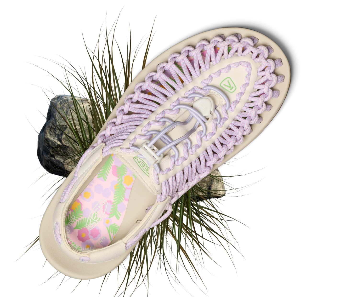 Product shot of lavender and cream uneek open-air sandal with grassy detail surrounding the product. 