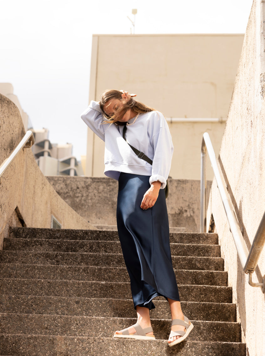Woman in black satin pants wearing tan Elle backstrap sandals while standing on city stairs. 