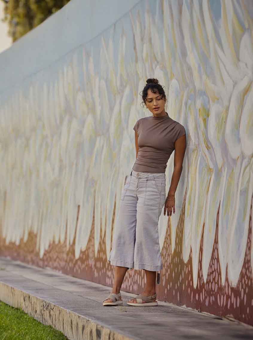 Woman wearing tan Elle Lux sandals while standing in front of flowery mural in a park.