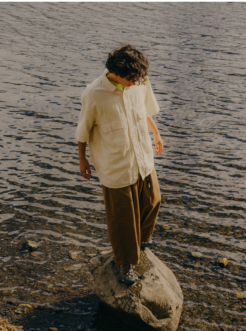 Man at a lake wearing brown Newport leather water sandal while standing on rock near the water's edge.