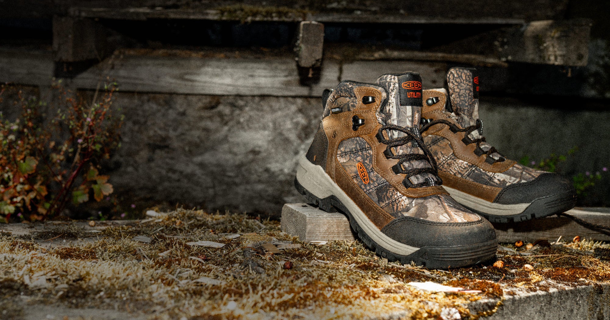Product shot of Skokie leather work boots with camo detail on mossy cement ledge in nighttime setting