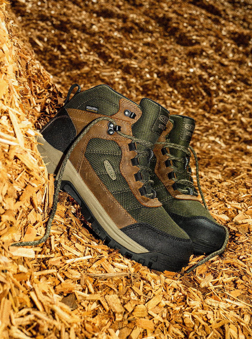Product shot of a pair of Skokie leather work boots in brown and green on pile of woodchips